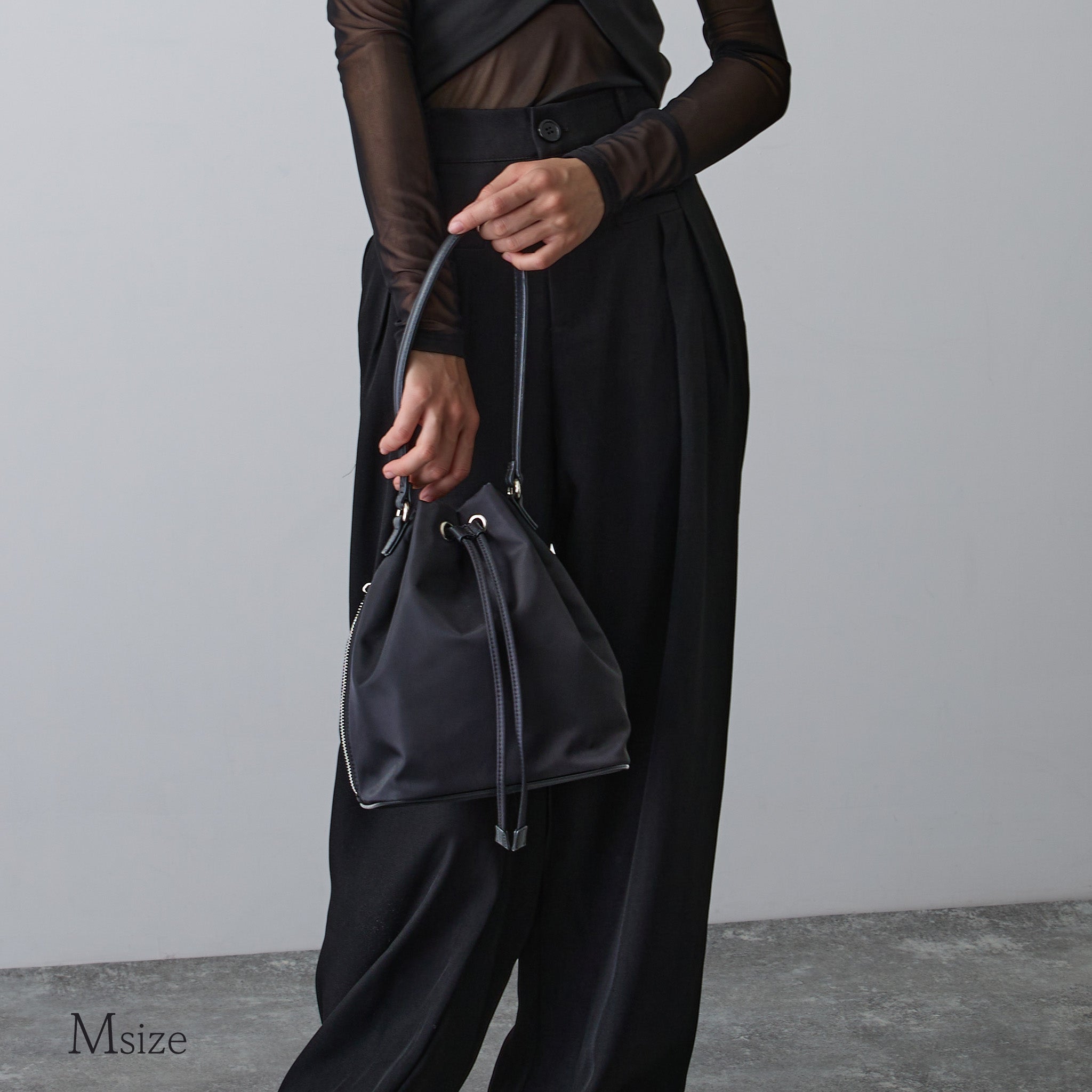 黒ナイロン巾着バッグMサイズを手に持つ女性 モード系スタイル