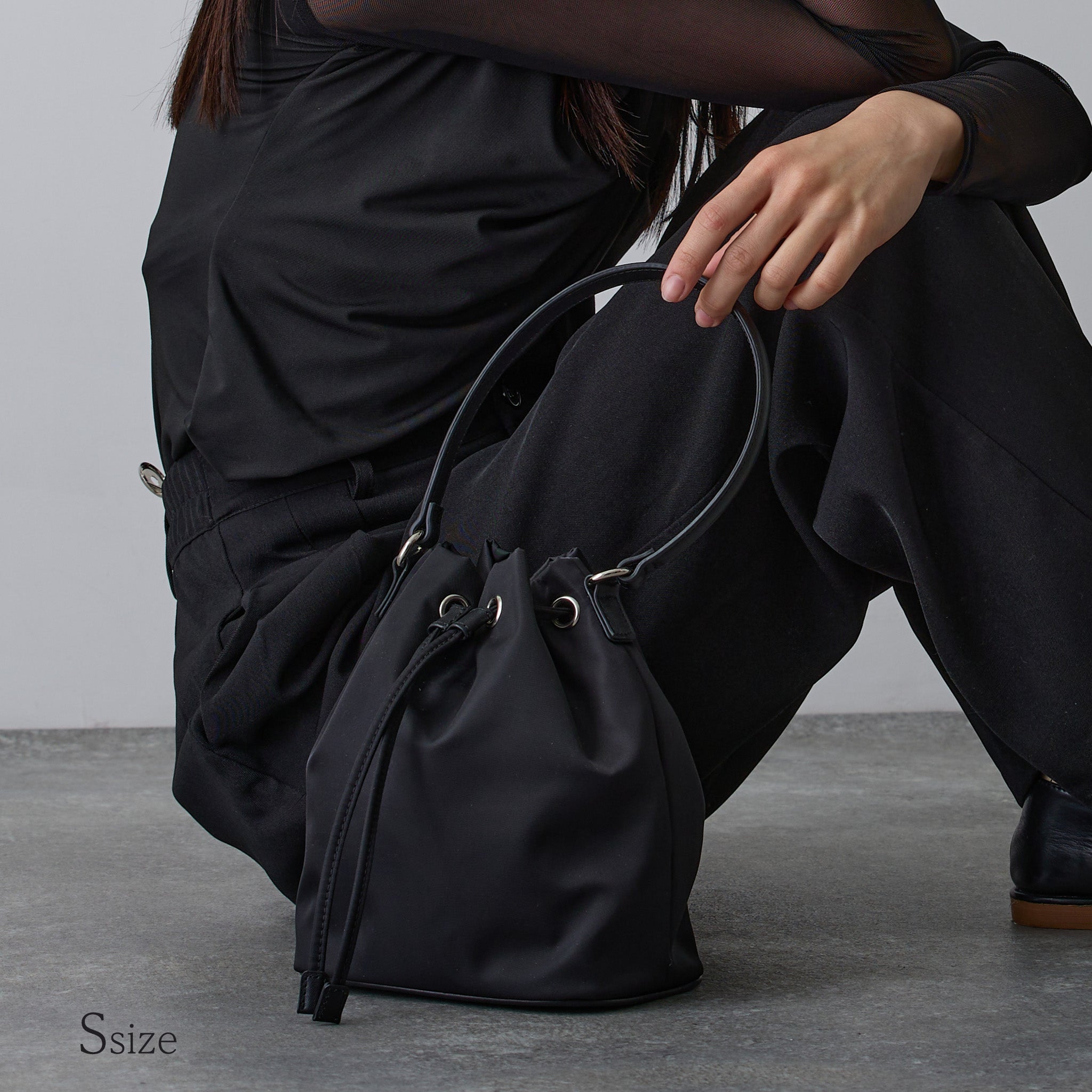 黒ナイロン巾着バッグSサイズを手に持つ女性 床に置いたスタイリング