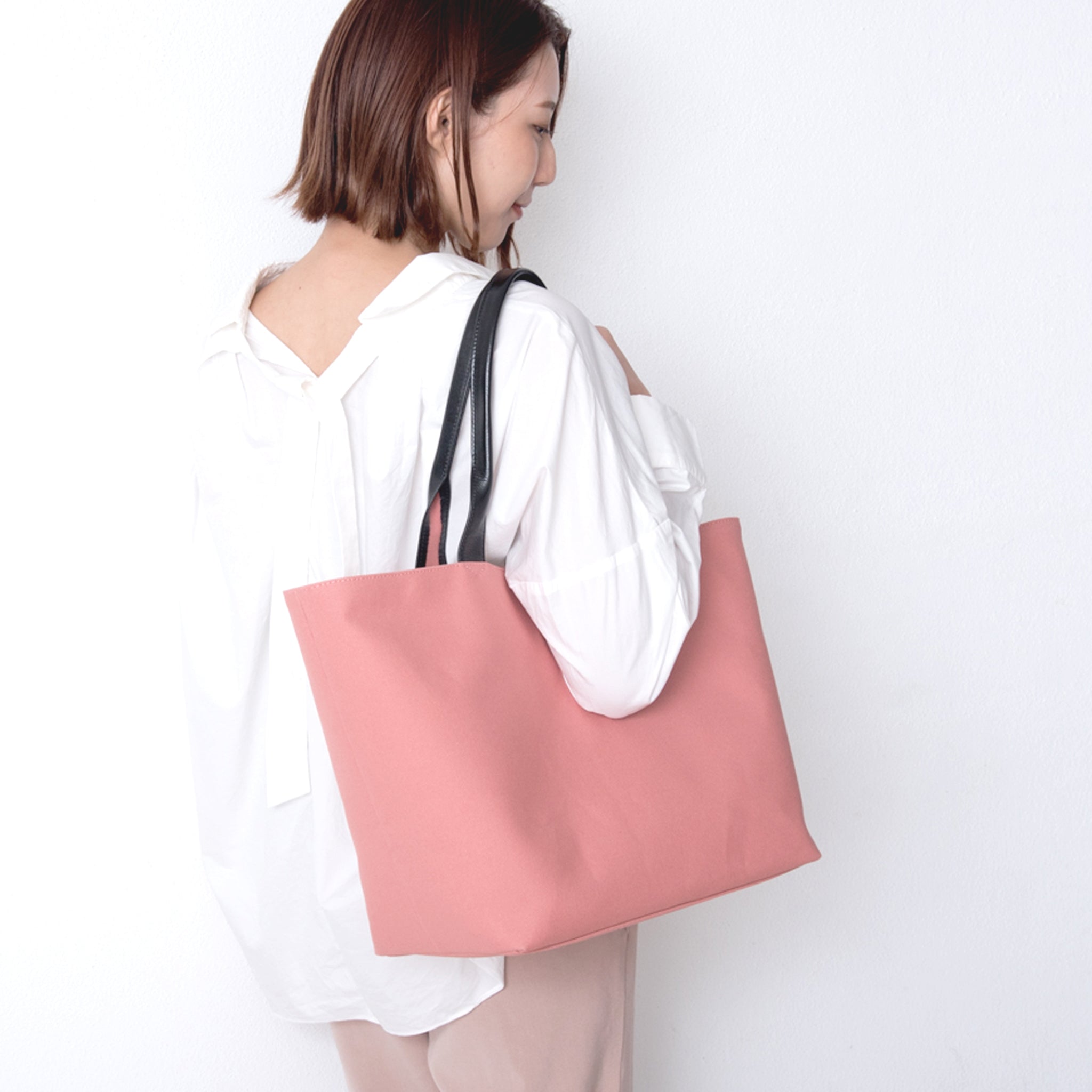 女性がピンクの帆布トートを肩にかけているところ